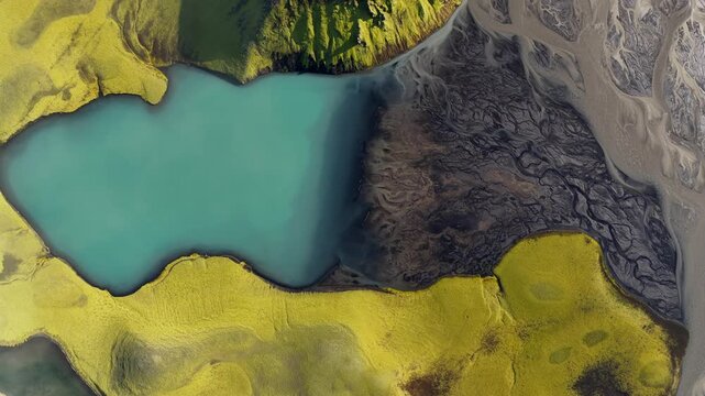 Aerial view of the turquoise Laki volcanic lake surrounded by vibrant green mossy lava fields and dark volcanic sediment patterns in Skaftarhreppur, Iceland.