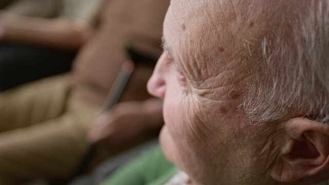 Side view detail shot of senior man sitting in retirement home, looking away, with focus on skin texture and wrinkles. Footage for senior care services and geriatric healthcare marketing campaigns