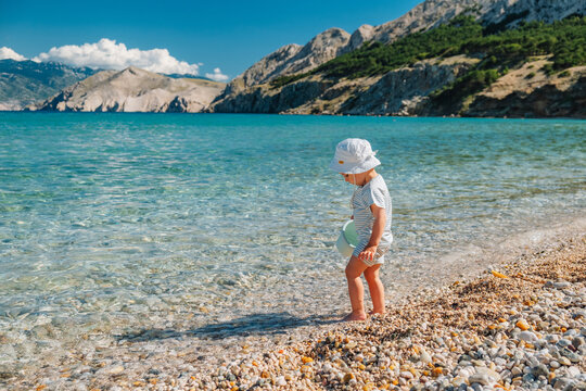 Toddler walking on pebble beach by turquoise lake