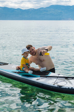 Father and toddler playing on paddleboard in clear lake