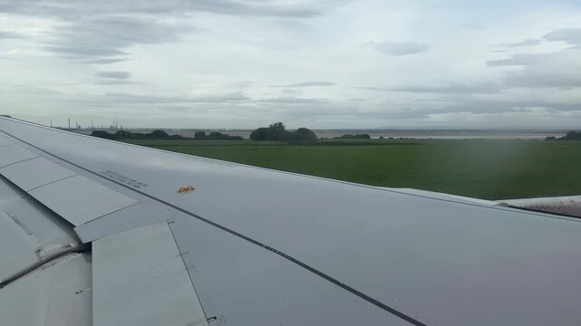Taking off and flying low in a passenger plane looking out of window at wing and landscape below England UK 4K
