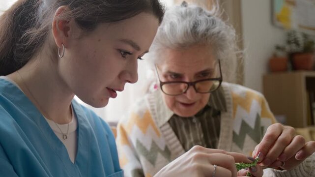 Close up shot of excited senior woman teaching young caregiver knitting in retirement home. Video for senior care service and nursing home promo