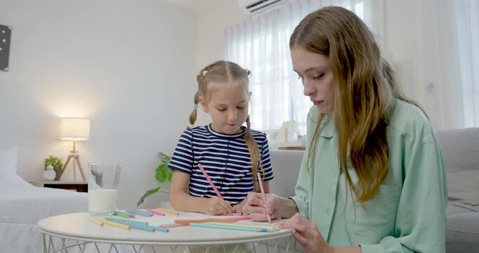 Caucasian single mother sits beside preschool daughter during drawing practice at cozy home table, offering gentle guidance, creative learning support, warm bonding for early childhood development