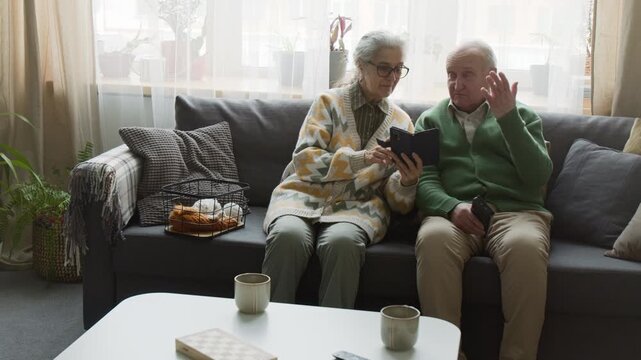 Senior couple sitting on sofa, using digital tablet and smartphone. Clip for marketing senior-friendly software, digital literacy courses, or retirement planning services
