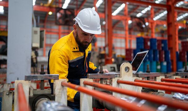 Industrial engineer in safety helmet uniform jacket working in heavy steel engineering factory. Technician manager worker inspector using laptop in metalwork product manufacturing facility workplace