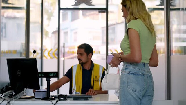 A female driver pays an attendant at a smart parking booth. This modern parking service scene shows vehicle pickup, secure transport, payment process and everyday urban mobility in a city facility.