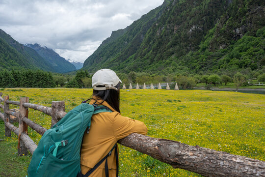 The female tourist is leaning against a wooden fence, taking in the view