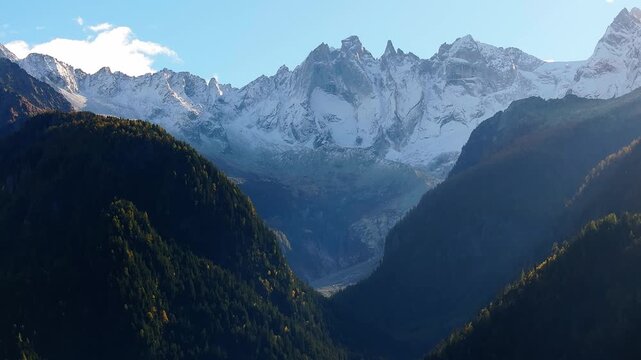 Aerial view of the snow-capped peaks of the Bregaglia Range rising above forested mountain slopes in Bregaglia, Grisons, Switzerland.