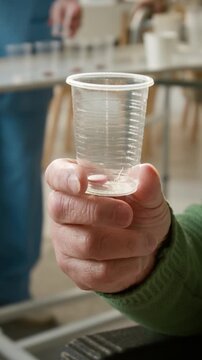 Unrecognizable senior patient holding plastic cup with pill in nursing home. Clip for healthcare, geriatric care, and pharmaceutical campaigns, vertical