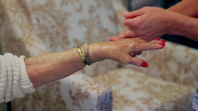 Beauty therapist gently moisturises and massages the hand of an elderly resident in a nursing home, highlighting personal care, wellbeing, dignity and compassionate aged care support. Close up.