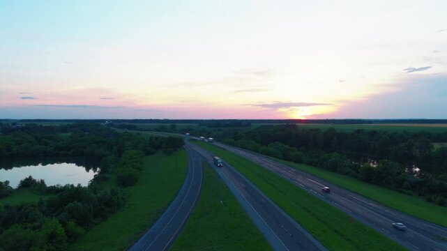 Interstate 64 stretching toward a pink sunset near Richview, Illinois, a divided highway and roadside lake glowing in warm summer evening light.
