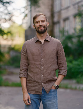 Smiling handsome bearded man in brown linen shirt standing outdoors on city street