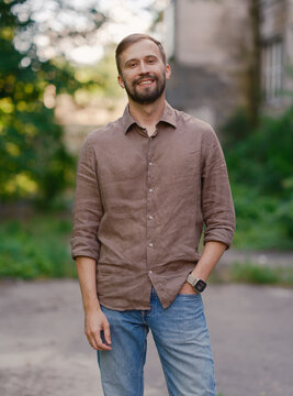 Smiling handsome bearded man in brown linen shirt standing outdoors on city street