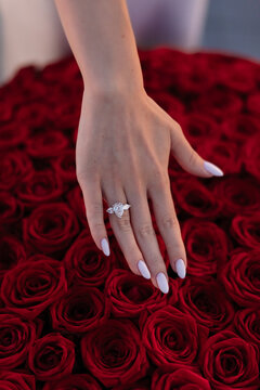 Woman hand showing diamond engagement ring over big bouquet of red roses