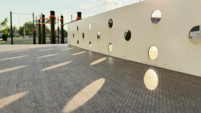 A sturdy ping pong table stands on an empty outdoor playground. Warm afternoon sunshine streams through the metal net, creating a deeply peaceful and nostalgic feeling.