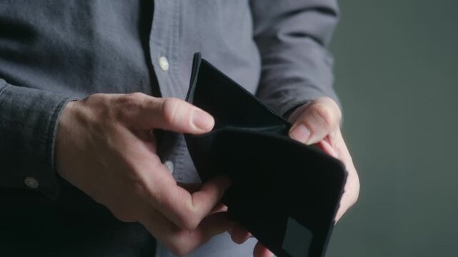 Closeup man hands opening empty black wallet, showing concept of being broke, unemployment, poverty, financial crisis, debt and having no money for payments. Broke man opening empty wallet no money