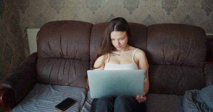 Front view of a focused young woman working on laptop while sitting on a sofa
