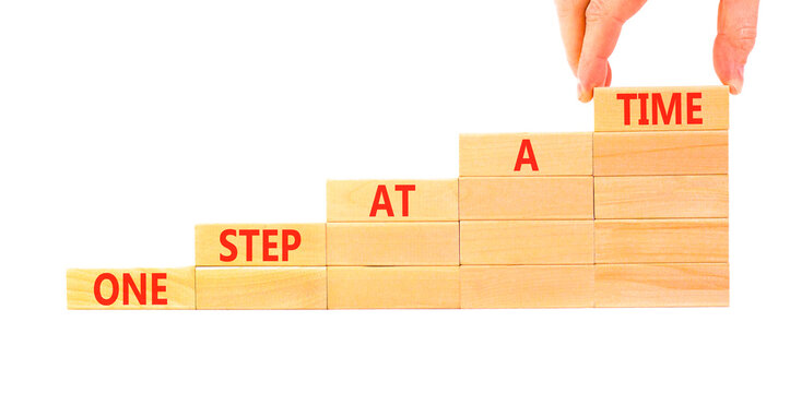 One step at a time symbol. Concept words One step at a time on beautiful wooden blocks. Beautiful white background. Businessman hand. Business and one step at a time concept. Copy space.