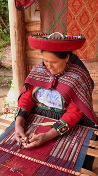 Indigenous Quechua woman weaving colorful threads on a traditional wooden loom in a rural village