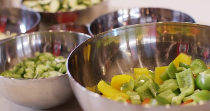 Multiple metal bowls filled with chopped fresh vegetables including zucchini peppers and cucumbers