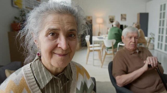 Close up portrait of senior woman smiling at camera in retirement home with senior man in background. Clip senior care facility marketing and geriatric healthcare promotions