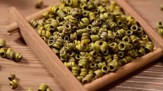 Close-up of dried Dendrobium officinale herbs in a wooden tray on a wooden surface