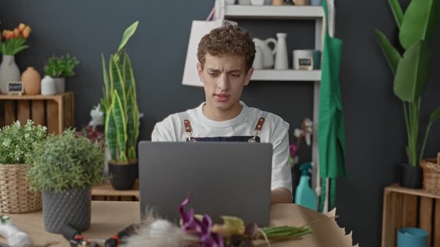 Man and woman florist in aprons lean over laptop, woman pointing at screen while man types in studio; collaboration focus.