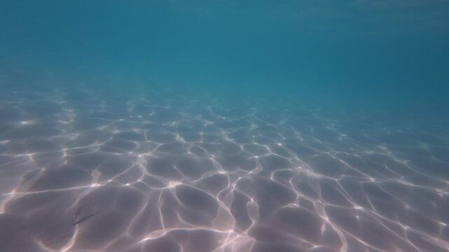 Underwater video of a sandy seabed beneath crystal clear Adriatic Sea water near Ba&scaron;ka on Krk Island, Croatia. Soft sunlight creates shimmering patterns across the sand