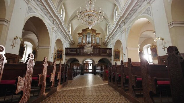 Moving through a Catholic Church, walking down the central aisle toward the door with the rear gallery above, holding a large pipe organ.