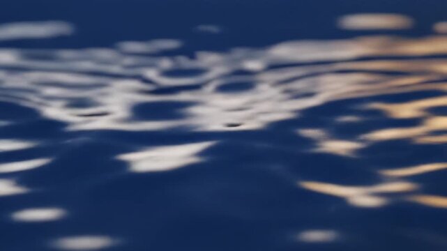 Ripples expanding on deep blue water surface with soft sunset reflections during a calm evening