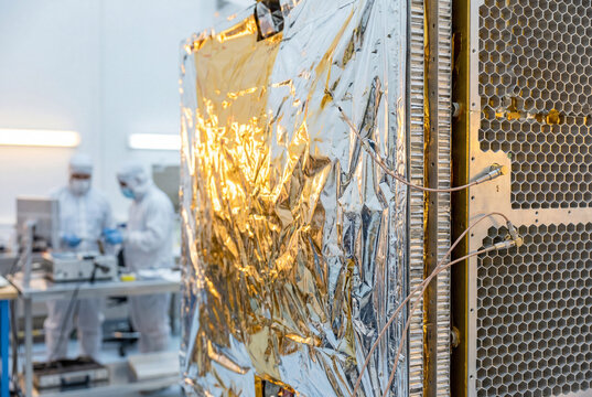 Satellite assembly inside cleanroom with engineers in protective suits