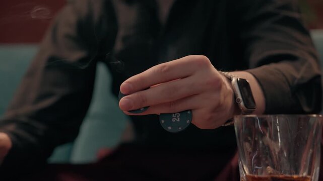 Close-up of a person holding poker chips & a cigar in a casino-style environment. Concept of gambling, betting, casino entertainment, risk taking, luxury lifestyle, gaming culture.