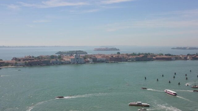 Public vaporettos and boats navigate the Venetian lagoon towards Giudecca island and the historic Zitelle church on a sunny day in Venice, Italy.