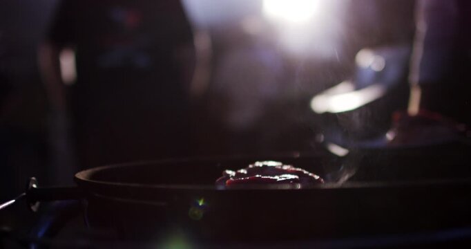 Close up view of hands in black glove shaping meat patty on grill during barbecue in dark environment