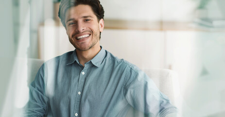 Obraz premium Smiling Young Caucasian Man Sitting In Office Chair At Home, Displaying Joyful Expression While Working. Bright Atmosphere With Relaxed Vibe, Symbolizing Business Concept.