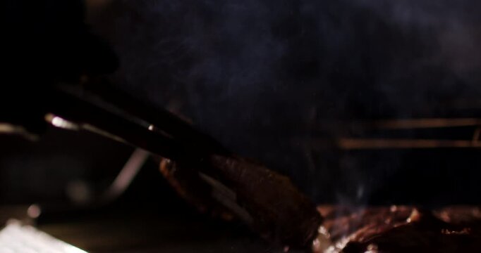 Close up view of hand using tongs to turn steak on hot grill causing bright fire flare and smoke