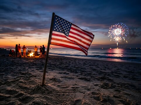 Group of people enjoying a beach bonfire with american flag and fireworks at sunset over the ocean