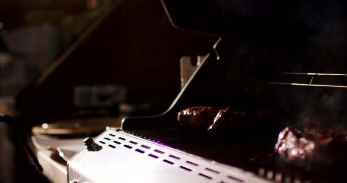 Close up shot of hand in black glove opening lid of barbecue grill with smoke rising