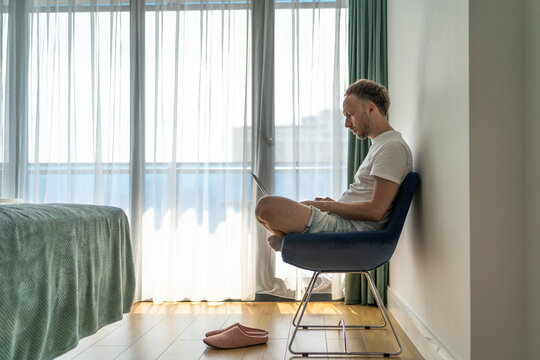 Remote work lifestyle man using laptop in bright apartment room, digital nomad workation, online business, home office interior.