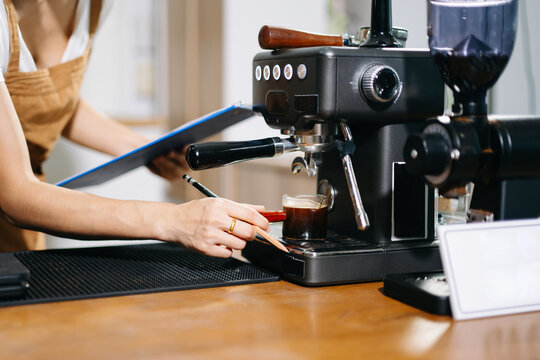 Barista writing order behind coffee machine and open sign on a warm wooden counter.
