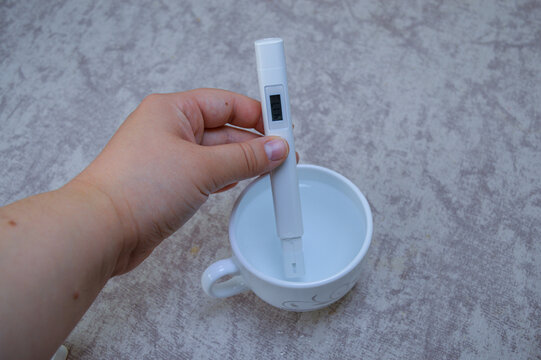 Digital TDS water tester held in a hand, measuring the purity of liquid in a white cup. Ideal for health, water quality, filtration, household testing, and scientific content.