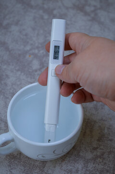 Digital TDS water tester held in a hand, measuring the purity of liquid in a white cup. Ideal for health, water quality, filtration, household testing, and scientific content.