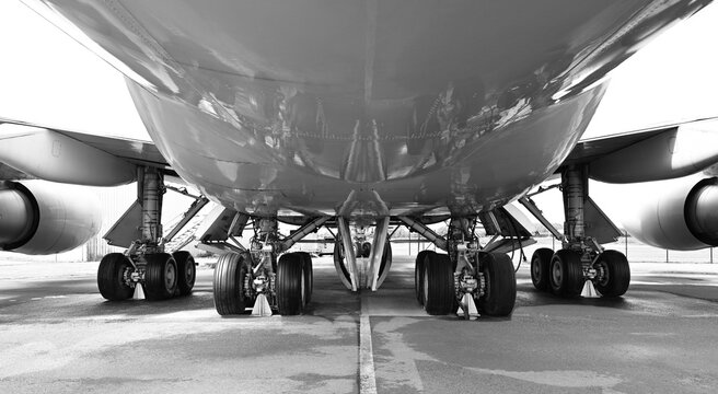 A black and white low-angle shot of airplane fuselage and landing gear on the runway tarmac.