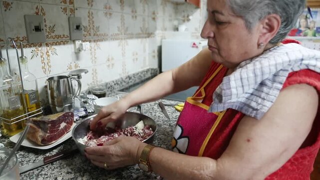  Mujer mayor mezclando ingredientes de alb&oacute;ndigas a mano en un taz&oacute;n. Abuela mayor amasando y mezclando ingredientes de alb&oacute;ndigas a mano en un taz&oacute;n. Cocina tradicional casera, aut&eacute;ntica senior.