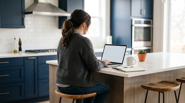 Woman working on a laptop at a kitchen island in a modern home