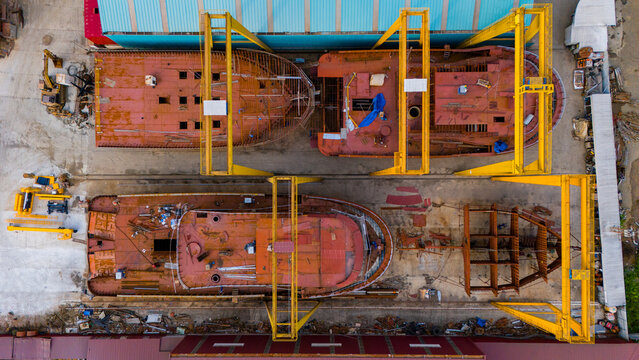 Aerial drone perspective directly above heavy industrial shipyard cranes and rusty boat frames