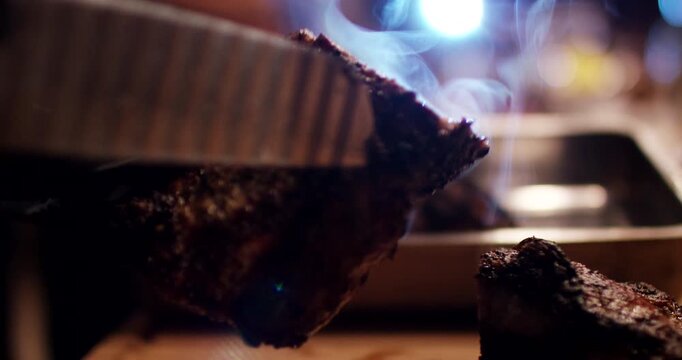 Close up shot of person in black glove holding piece of roasted meat with steam rising