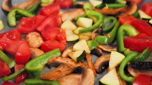 Vegetables including tomatoes, peppers, and mushrooms are sizzling in a hot skillet, creating a colorful and aromatic cooking scene in a kitchen. High quality 4k footage