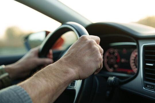 Male hands holding steering wheel while driving