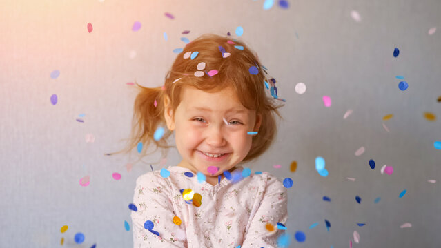 Little girl smiling and cheering with open eyes, enjoying a festive celebration as colorful circular paper confetti falls around her, creating a joyful and energetic atmosphere